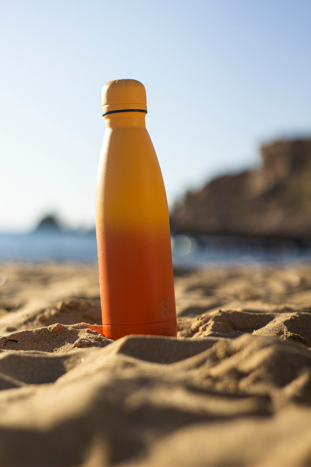Orange and yellow Water Bottle Sitting On The Golden Sands Beach in Malta.