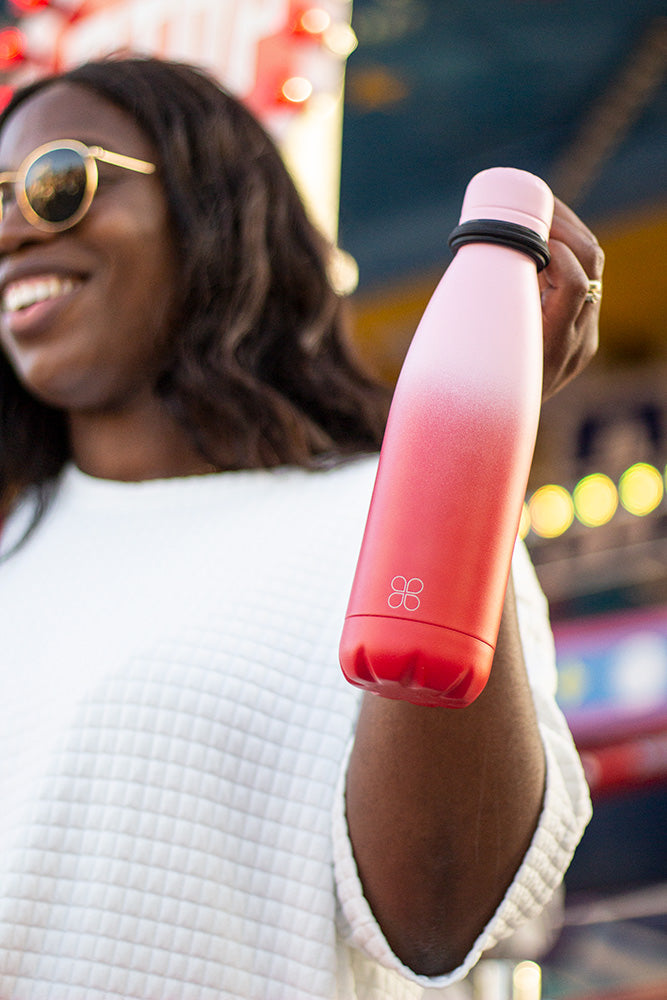 Lady in sunglasses holding up a pink and red stainless steel water bottle