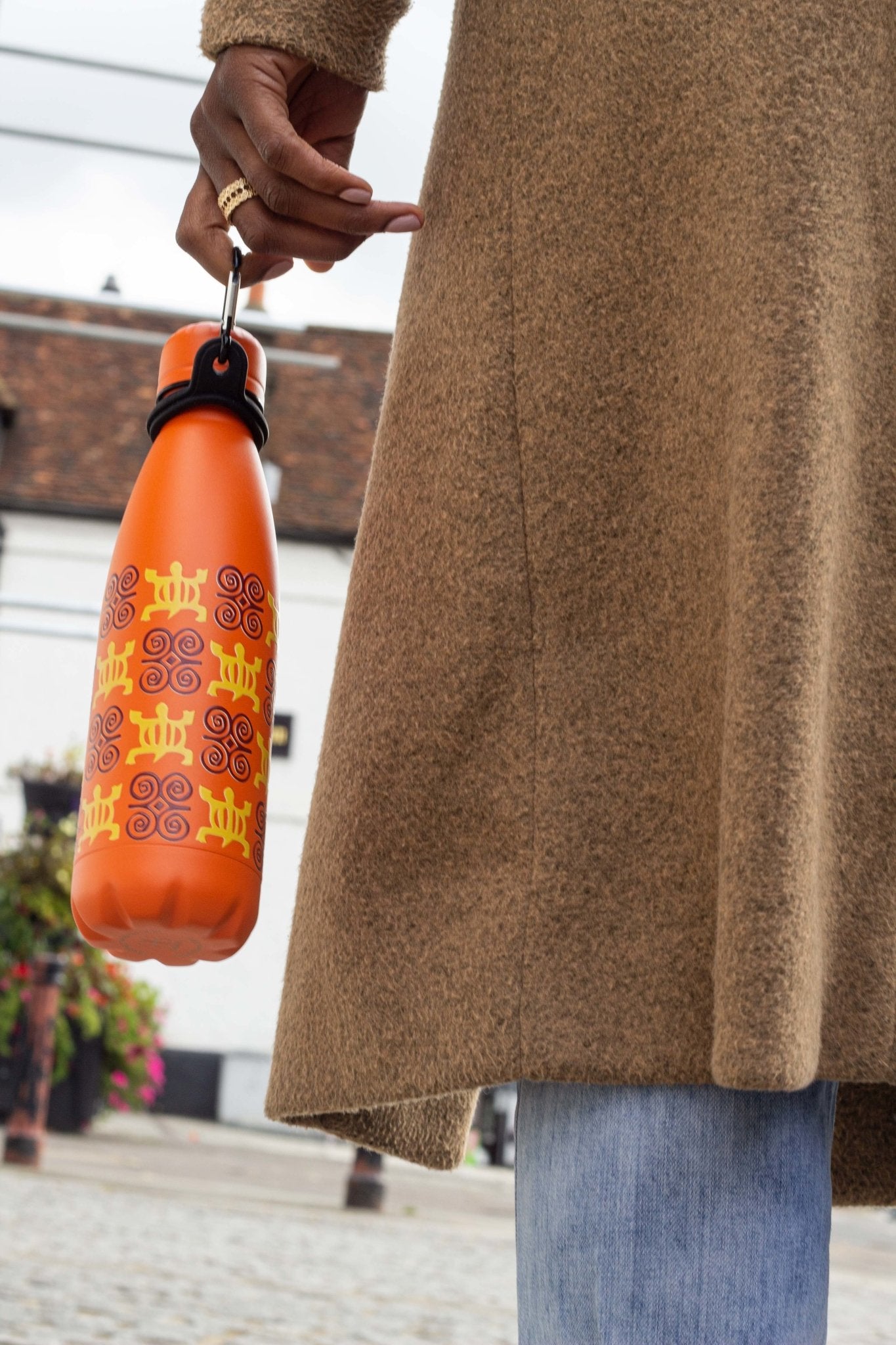 Orange bottle with Adinkra design held by caribaner