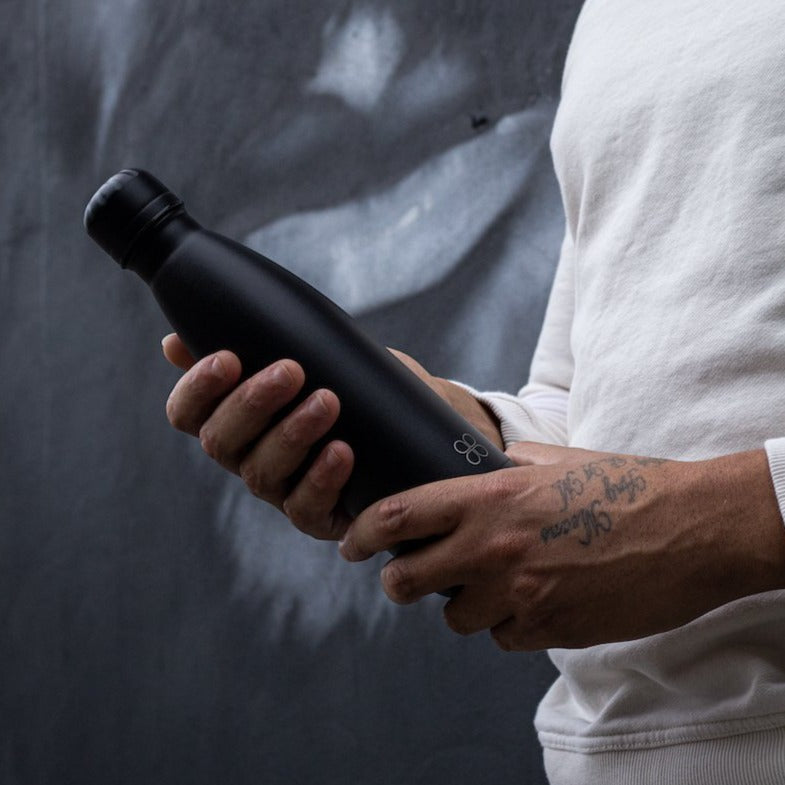 Man holds a black metal water bottle in front of a mural.