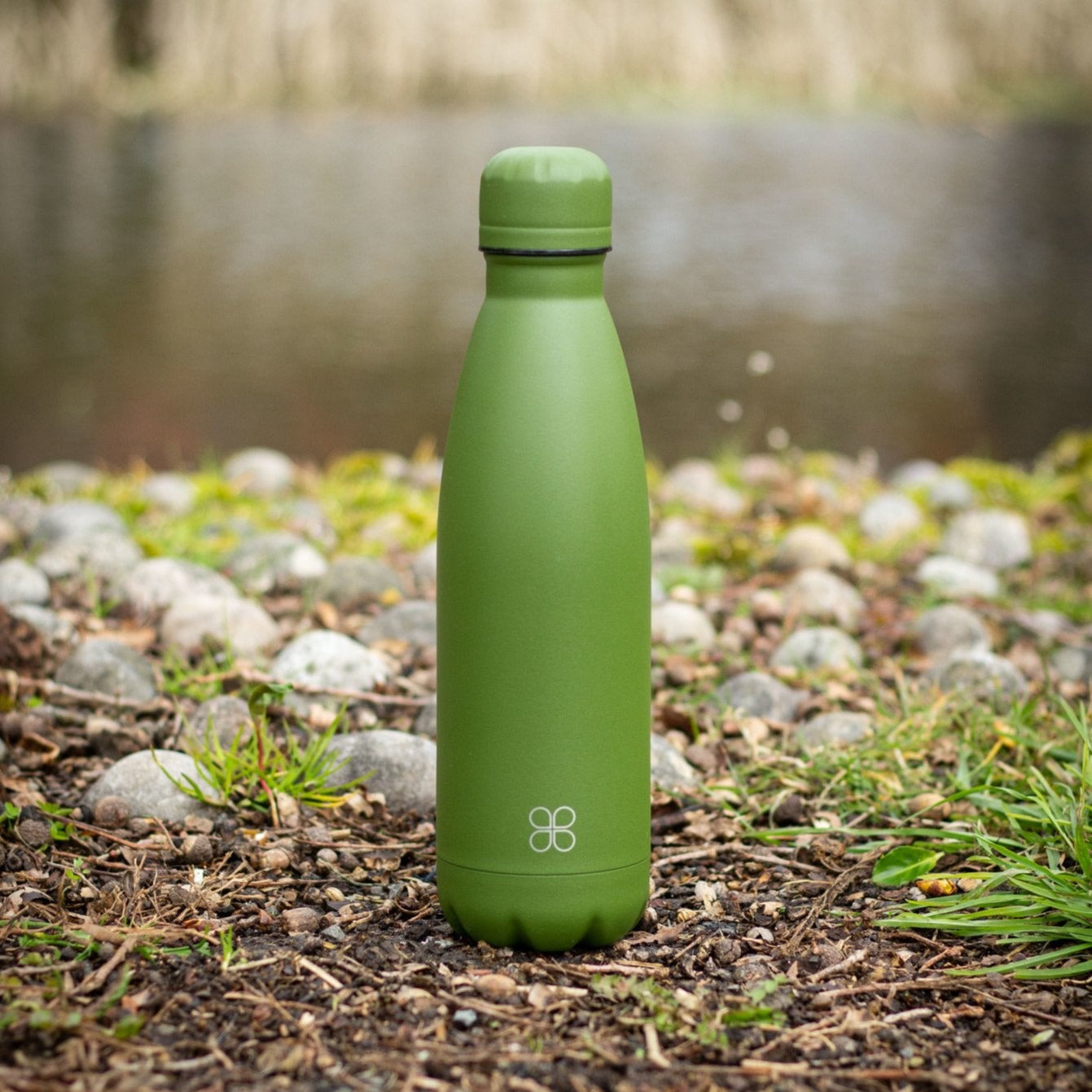 A Forest Green water bottle sits at the edge of a pond in a park.