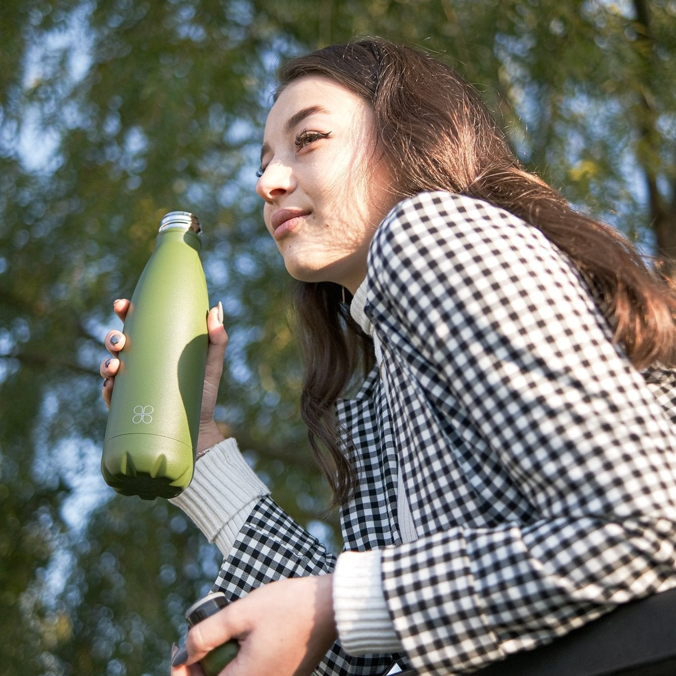 Lady in black and white chequered jacket smiles while she holds a forest green water bottle.